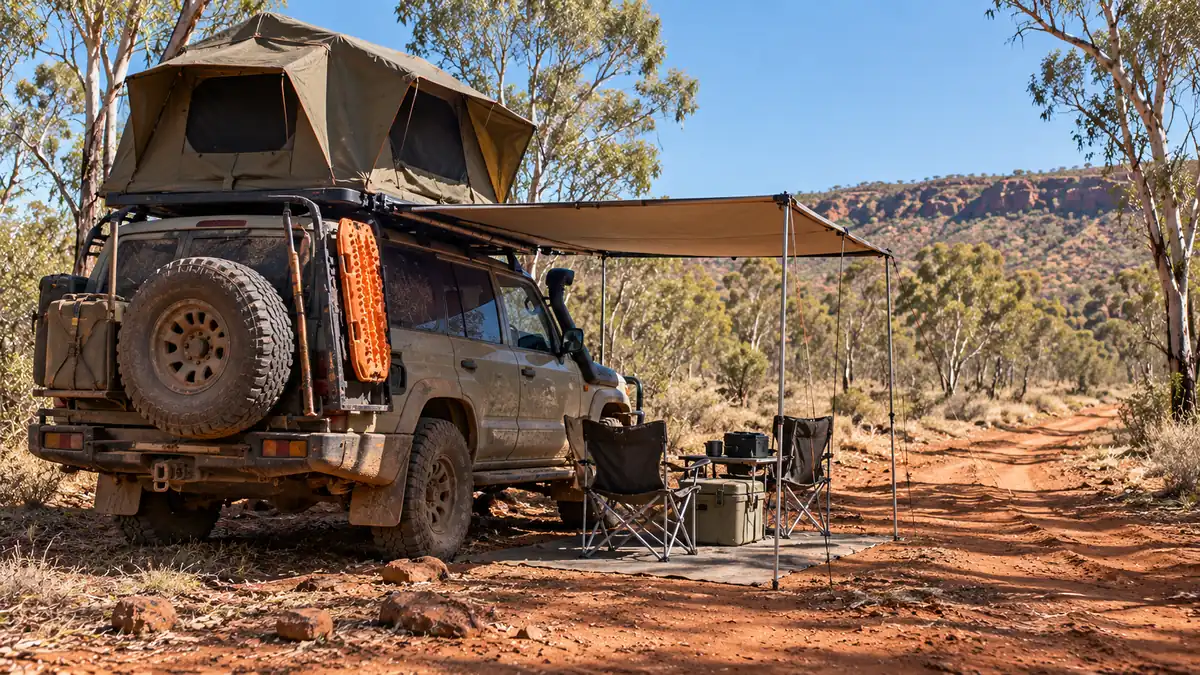 4WD with rooftop tent, orange recovery boards and awning on a red dirt track